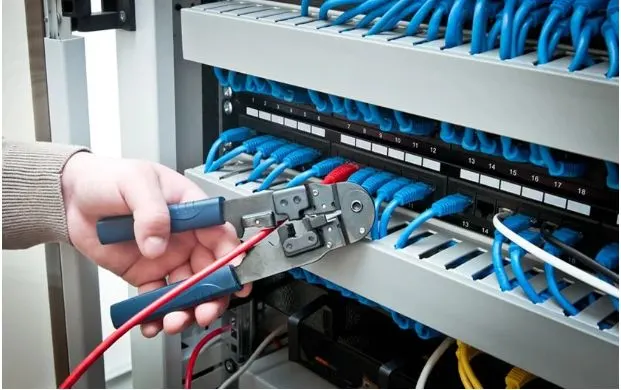 Technician terminating a network cable on a patch panel with a punch down tool